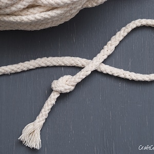May include: A close-up of a white cotton rope with a knot tied in it. The rope is lying on a dark grey surface.