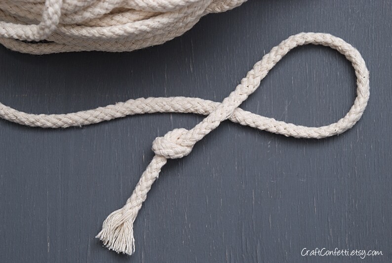 May include: A close-up of a white cotton rope with a knot tied in it. The rope is lying on a dark grey surface.