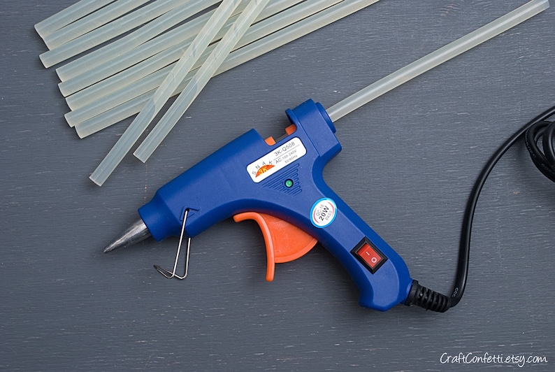 May include: A blue and orange hot glue gun with a black cord and a clear glue stick. The glue gun has a power switch and a temperature control dial. The glue stick is 20W.