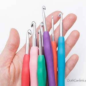 May include: A set of six colorful crochet hooks with metal tips. The hooks are arranged in a hand, with the largest hook at the top and the smallest hook at the bottom.