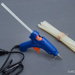 May include: A blue hot glue gun with an orange trigger and a clear glue stick. A bundle of clear glue sticks is tied together with twine.