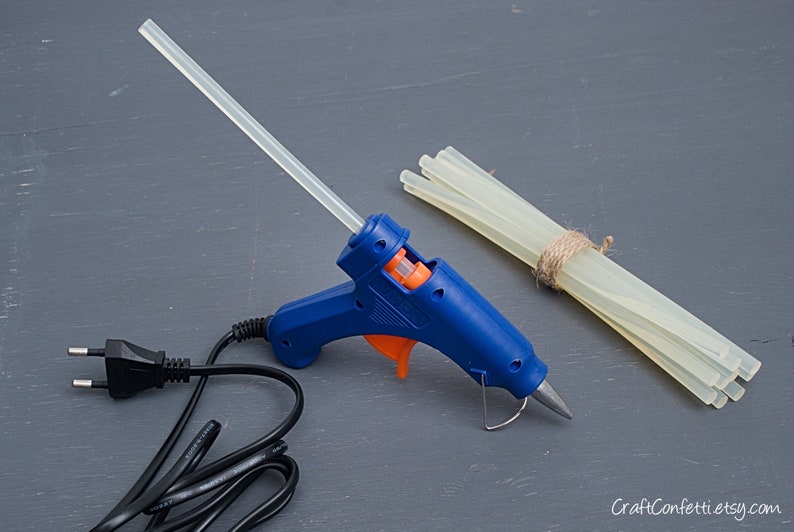 May include: A blue hot glue gun with an orange trigger and a clear glue stick. A bundle of clear glue sticks is tied together with twine.