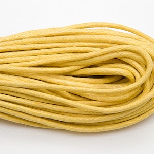 May include: A close-up of a spool of yellow cotton cord. The cord is tightly wound and has a smooth texture.