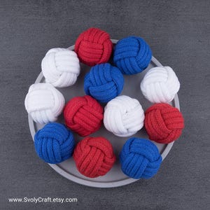 May include: A selection of red, white, and blue nautical rope balls displayed on a grey plate. The tightly knotted balls have a textured appearance. The Etsy shop URL is visible at the bottom of the image.
