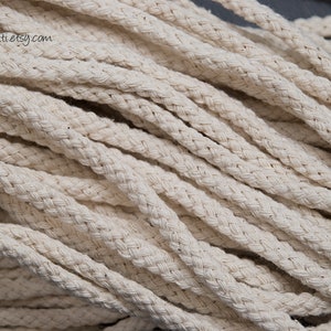 May include: Close-up of a pile of natural white cotton rope. The rope is braided and has a soft, textured surface.