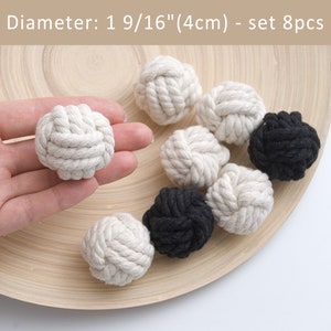 May include: A collection of eight decorative rope knot balls in off-white and black. Each ball is approximately 4 cm in diameter. The balls are displayed on a light wooden surface.