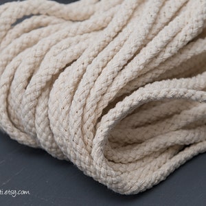 May include: Close-up of a thick, natural-coloured cotton rope. The rope is tightly wound and has a soft, textured surface.