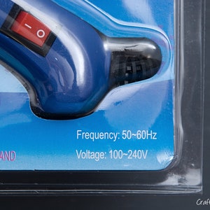 May include: Close-up of a blue and black glue gun with a red on/off switch. The packaging indicates a frequency of 50-60Hz and a voltage of 100-240V.