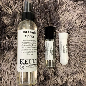 May include: Three glass bottles containing essential oil blends for hot flashes. The bottles are labeled "Hot Flash Spritz", "Hot Flash Roll On", and "Hot Flash Inhaler". The bottles are on a gray fuzzy surface.