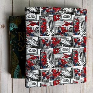 May include: A book cover with a comic strip design featuring Spider-Man in red, blue, and white. The cover is wrapped around a book with a dark cover and gold lettering. The comic strip design includes speech bubbles.