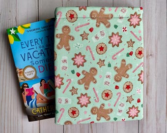 May include: A green book sleeve with a repeating pattern of gingerbread men, candy canes, and snowflakes. The book sleeve is made of fabric and has a drawstring closure.