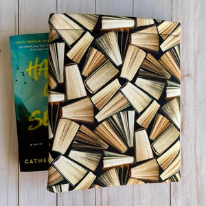 Peut inclure: Une housse de livre avec un fond noir et un motif de livres empilés avec des pages ouvertes dans des tons de brun et de crème.