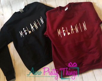 Puede incluir: Dos sudaderas con la palabra "MELANIN" escrita en una fuente estilizada, similar al logotipo de "Friends". Una sudadera es negra y la otra es burdeos.