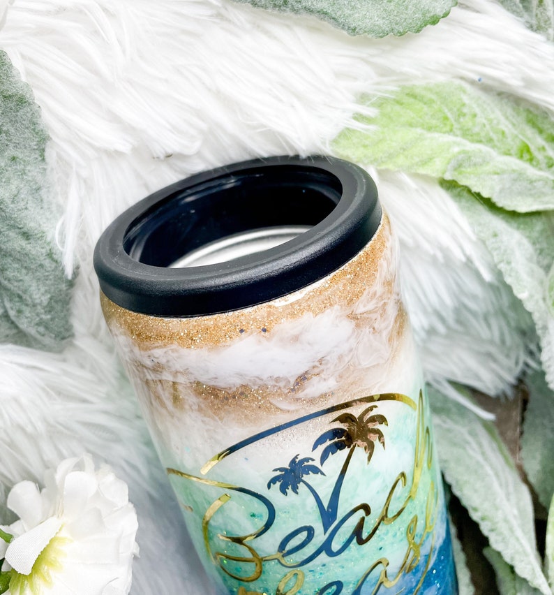 May include: A tumbler with a black rim and a beach-themed design. The tumbler features a gold glitter band, white and blue swirls, and a gold palm tree graphic with the words "Beach Please".