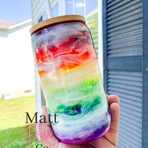 May include: A clear glass tumbler with a rainbow design, a bamboo lid, and a glass straw. The tumbler has a vibrant blend of colours, including red, orange, yellow, green, blue, and purple. The text "Matt Five Co." is printed on the side.