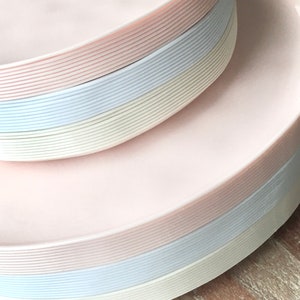 May include: Stack of pink, white, and light blue disposable plastic plates. The plates are stacked in a pyramid shape.