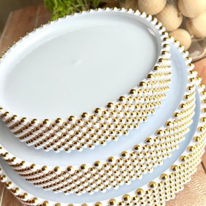 May include: Three white round cake stands with gold bead trim. The stands are stacked on top of each other.