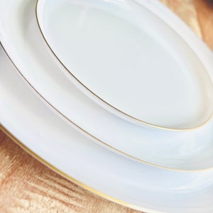 May include: Three white ceramic plates with a gold rim. The plates are stacked on top of each other.