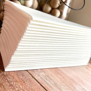 May include: A stack of white paper towels, folded and neatly arranged. The towels are on a wooden surface.