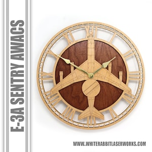 May include: A wooden wall clock featuring a detailed silhouette of an E-3A Sentry AWACS aircraft. The clock face has Roman numerals and the aircraft is centered on the clock face. The clock is made of light wood with a dark wood center.