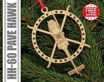 May include: A wooden Christmas ornament featuring a detailed silhouette of a HH-60 Pave Hawk helicopter surrounded by a circle of stars. The ornament is attached to a red ribbon.