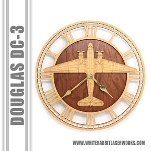 May include: A wooden clock featuring a Douglas DC-3 airplane design. The clock face has Roman numerals and the airplane is centered on the clock face. The clock is made of light wood with a dark wood center.