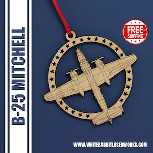 May include: A wooden ornament shaped like a B-25 Mitchell bomber plane, surrounded by a circle of stars. The ornament is a light brown color and has a red ribbon attached to the top.