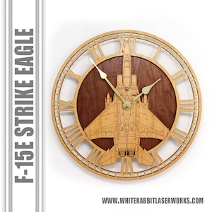 May include: A wooden wall clock with Roman numeral markings and a laser-cut design of an F-15E Strike Eagle fighter jet. The clock face is made of a dark wood and the hands are gold.