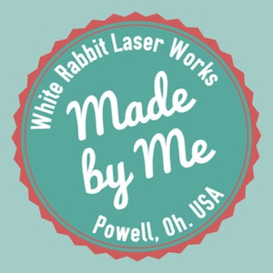 K&ouml;nnte beinhalten: Rundes Logo in T&uuml;rkis und Rot mit dem Text "White Rabbit Laser Works" am Rand. Die Worte "Made by Me" sind in Schreibschrift, mit "Powell, Oh. USA" unten.