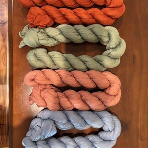 May include: Four braided fabric scarves in different colors: rust, sage green, dusty rose, and light blue.