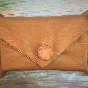 May include: A brown fabric envelope clutch with a wooden button closure. The clutch has a flap that folds over and is secured with the button.