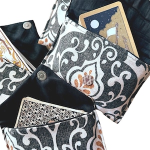 Può includere: Tre pochette in tessuto con motivo bianco e nero con fodera in tessuto nero e chiusura a scatto. Ogni pochette contiene una carta dei tarocchi.