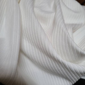 May include: White ribbed fabric with a soft, textured surface. The fabric is folded and draped, showing the texture and drape of the material.