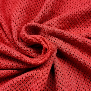 Puede incluir: Primer plano de una tela roja vibrante con una textura similar a una malla. El material está tejido apretadamente con pequeños agujeros espaciados uniformemente, creando un textil transpirable y flexible. La tela está recogida y doblada.