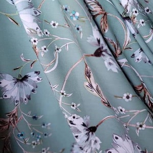 May include: A light blue fabric with a white floral pattern. The fabric has a soft, flowing texture and is ideal for creating garments or home decor.