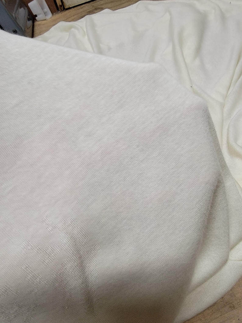 以下が含まれることがあります： 滑らかな質感の白い布のシート。シートは折り畳まれており、わずかに光沢があります。