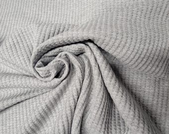 May include: Gray waffle knit fabric with a textured surface. The fabric is folded and twisted, showing the texture and drape.