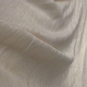 Op de afbeelding: Close-up van een witte stof met een textuur geweven. De stof is zacht en drapeert mooi.