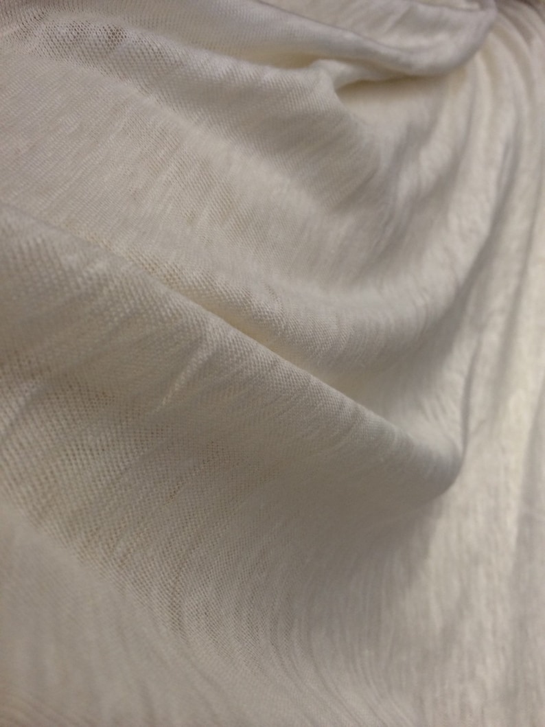 Op de afbeelding: Close-up van een witte stof met een textuur geweven. De stof is zacht en drapeert mooi.