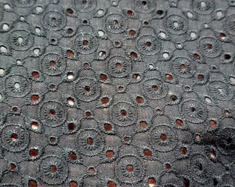 May include: Close-up of black eyelet fabric. The fabric features a repeating pattern of floral-shaped cutouts, creating a delicate and airy texture. The eyelets are evenly spaced, and the fabric appears to be a lightweight material, suitable for clothing.