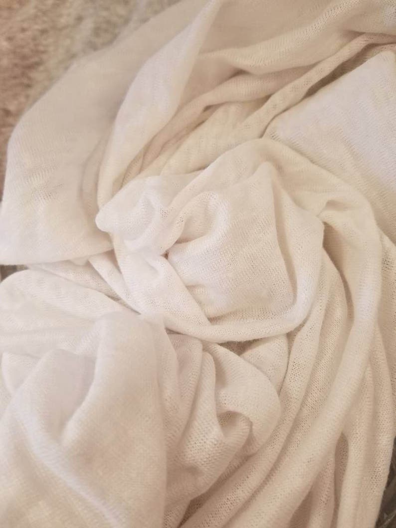 Puede incluir: Tela blanca con una superficie suave y texturizada. La tela est&aacute; drapeada y doblada, creando un aspecto suave y fluido.