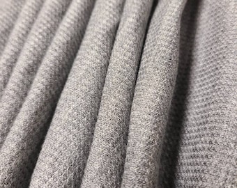 May include: Close-up of a gray, textured fabric with a subtle herringbone pattern. The fabric is folded in a series of pleats, creating a soft and inviting look.