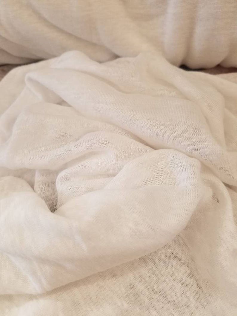 Puede incluir: Tela de lino blanca con una superficie suave y texturizada. La tela est&aacute; doblada y drapeada, creando un aspecto suave y fluido.