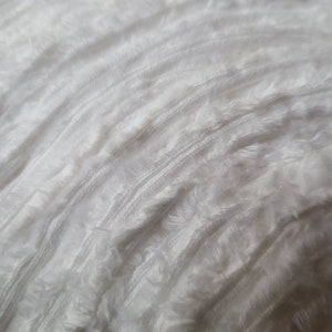May include: White fluffy yarn with a textured, slightly bumpy surface.