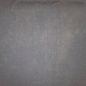 May include: Close-up of a textured, navy blue fabric with vertical ribbing. The fabric has a subtle sheen and a slightly worn appearance, with lighter areas interspersed throughout the darker blue.