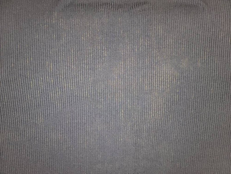 May include: Close-up of a textured, navy blue fabric with vertical ribbing. The fabric has a subtle sheen and a slightly worn appearance, with lighter areas interspersed throughout the darker blue.