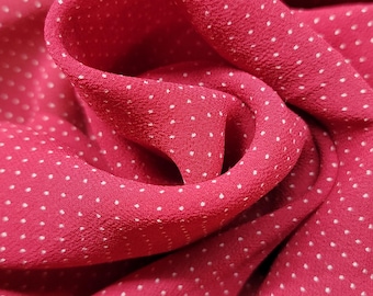 May include: Close-up of a pink fabric with a white polka dot pattern. The fabric is folded and draped, showing its texture and the pattern.