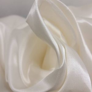 May include: Close-up of a smooth, ivory white satin fabric, draped and folded to show its texture and sheen.