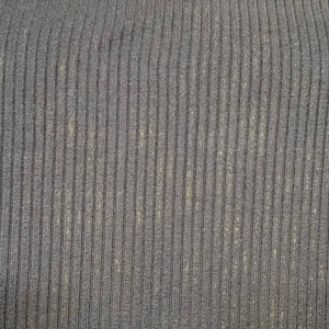 May include: Close-up of a dark gray ribbed knit fabric. The fabric has vertical lines and a slightly textured appearance. There are subtle flecks of a lighter color throughout the material, adding visual interest to the textile.