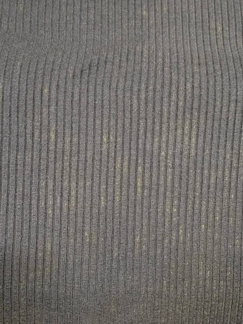 May include: Close-up of a dark gray ribbed knit fabric. The fabric has vertical lines and a slightly textured appearance. There are subtle flecks of a lighter color throughout the material, adding visual interest to the textile.